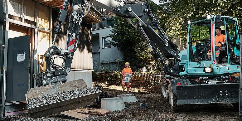 Kolové rypadlo Wacker Neuson EW100 manipuluje na staveništi s sypkým materiálem pomocí naklápěcí lopaty.