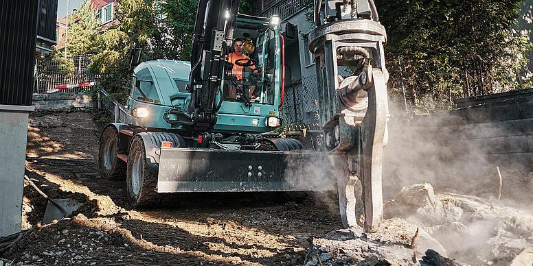 Wacker Neuson EW100 wheeled excavator using a hydraulic breaker for demolition work in a confined residential area.