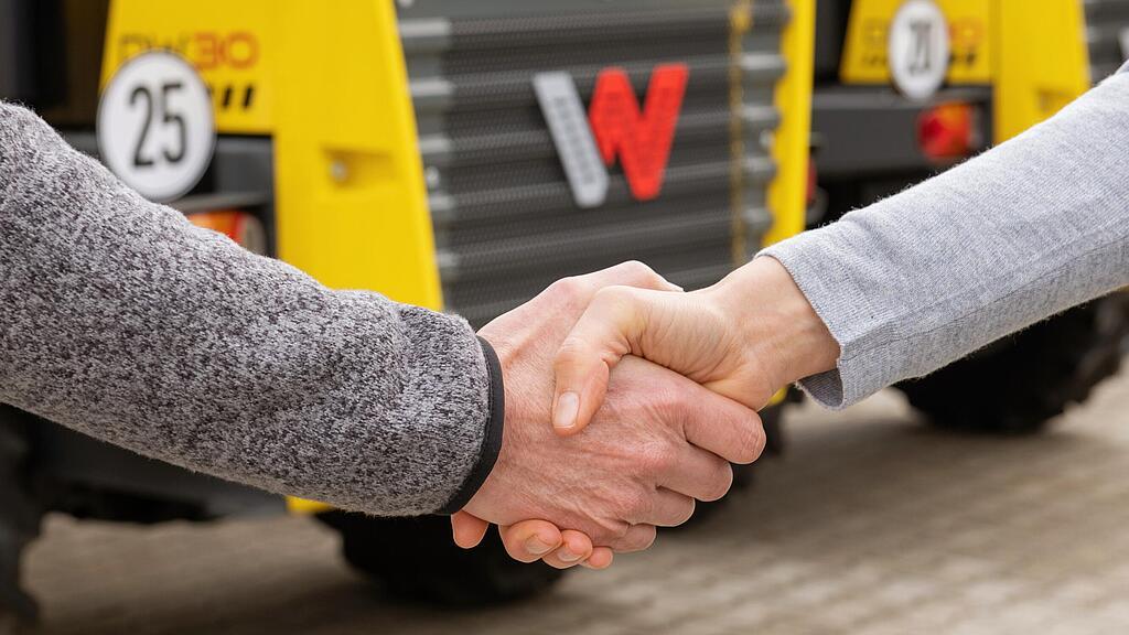 Podání rukou mezi zaměstnankyní Wacker Neuson a zákazníkem, v pozadí stavební stroje Wacker Neuson.