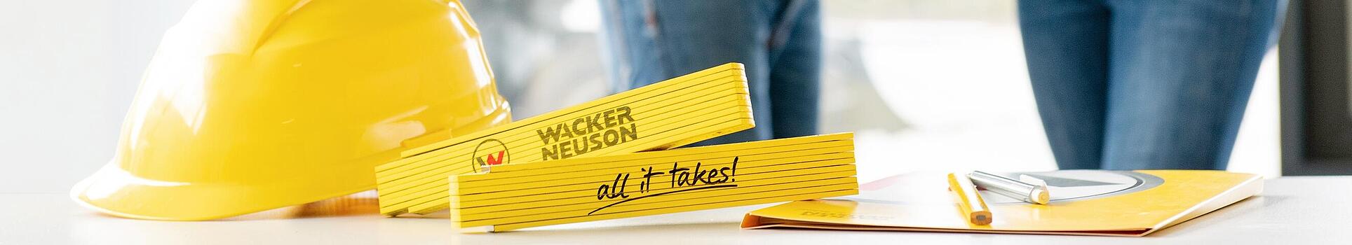 Zboží Wacker Neuson je na stole v popředí a zaměstnanci Wacker Neuson v pozadí.