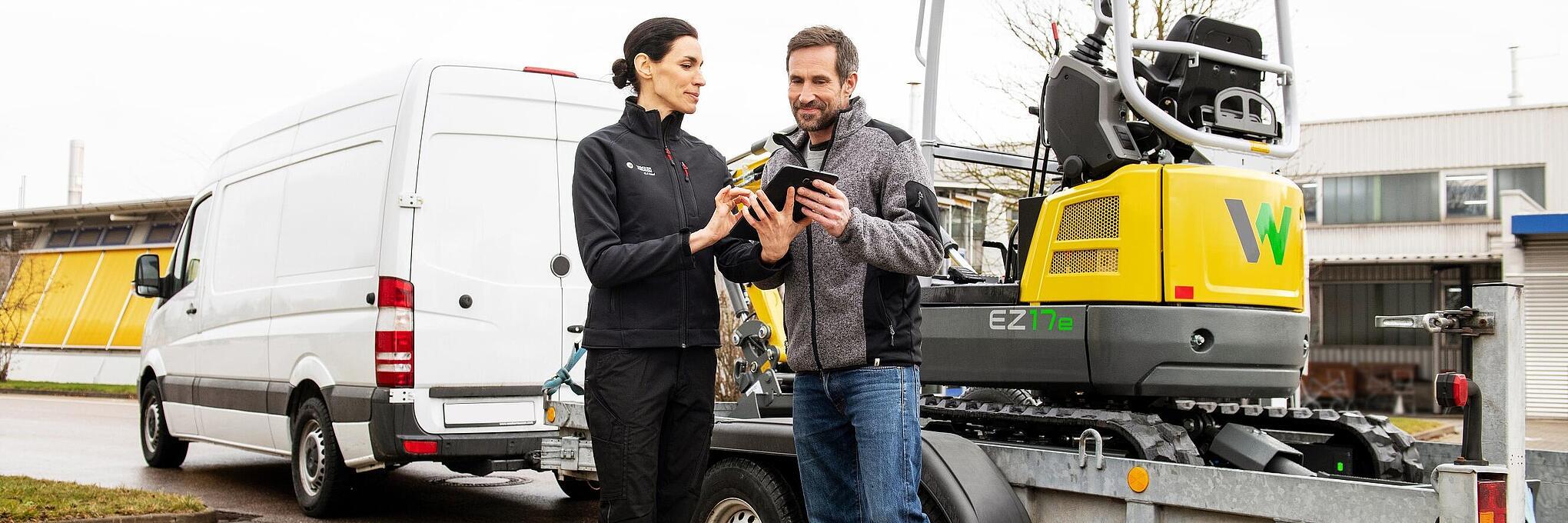 Wacker Neuson employee and customer in front of rented zero emission tracked excavator on a trailer.