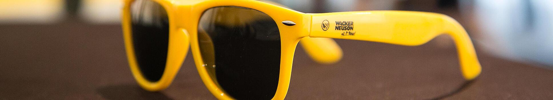 Žluté sluneční brýle s logem Wacker Neuson.