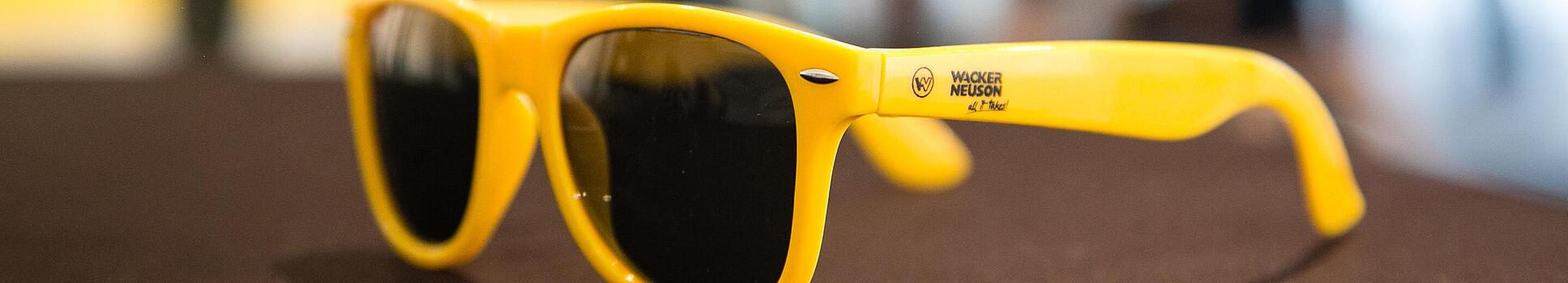 Yellow sunglasses with Wacker Neuson logo.