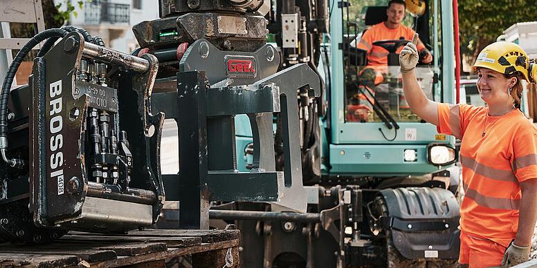 Obsluha připravuje hydraulické příslušenství na kolovém rypadle Wacker Neuson EW100 na staveništi v městském prostředí.