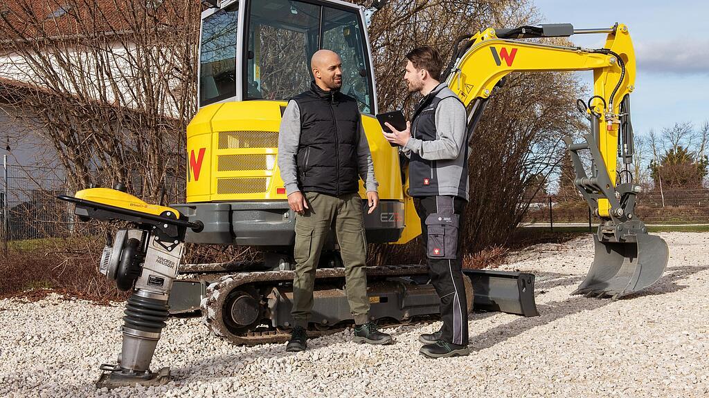 Zaměstnanec společnosti Wacker Neuson radí zákazníkovi ohledně balíčku WeCare před stroji Wacker Neuson.